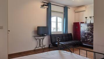 A bedroom with a bed, a TV on a small table, a sofa, and a cabinet with decorative panels.