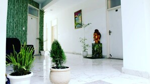 Un vestíbulo amplio con piso de mármol, plantas en macetas, una estatua de Buda y un cuadro en la pared.