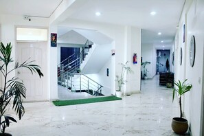 A spacious lobby with a marble floor, a staircase, and potted plants. - Hotel Noida Stay (Noida)