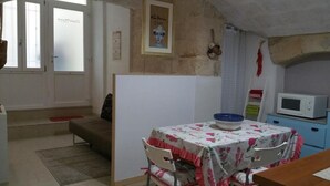 A small kitchen with a microwave, a table with a floral tablecloth, and a chair. - Quad room (Monopoli)