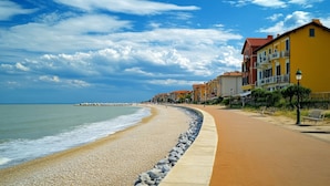 A coastal walkway with pebbles, a sandy beach, and buildings with balconies. - Bright Studio Near the sea in Caorle (Caorle)