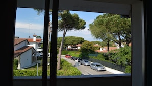A residential street view through a window, featuring houses with red-tiled roofs, parked cars, and lush greenery. - Bright Studio Near the sea in Caorle (Caorle)