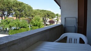 A balcony with a white plastic chair, a metal rack, and a view of trees and buildings. - Bright Studio Near the sea in Caorle (Caorle)