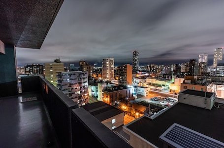 Vista nocturna de una ciudad con edificios altos y un estacionamiento visible desde un balcón.