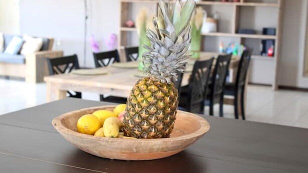 Un saladier en bois sur une table, avec un ananas et des citrons.