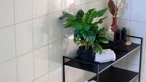 Une étagère d’angle avec une plante en pot, un vase de fleurs et des serviettes pliées.
