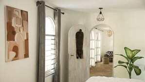 Une chambre à coucher avec un lit, une plante et un couloir menant à une autre pièce.