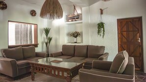 Un salon avec un canapé d’angle, une table basse en verre, des plantes suspendues et une porte en bois.