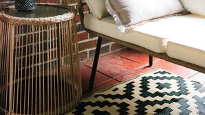 Un coin accueillant avec un fauteuil en osier, un banc rembourré, une plante en pot et un tapis à motifs.