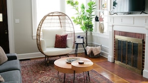 Un salon avec un fauteuil en osier, un canapé, une cheminée et un téléviseur.