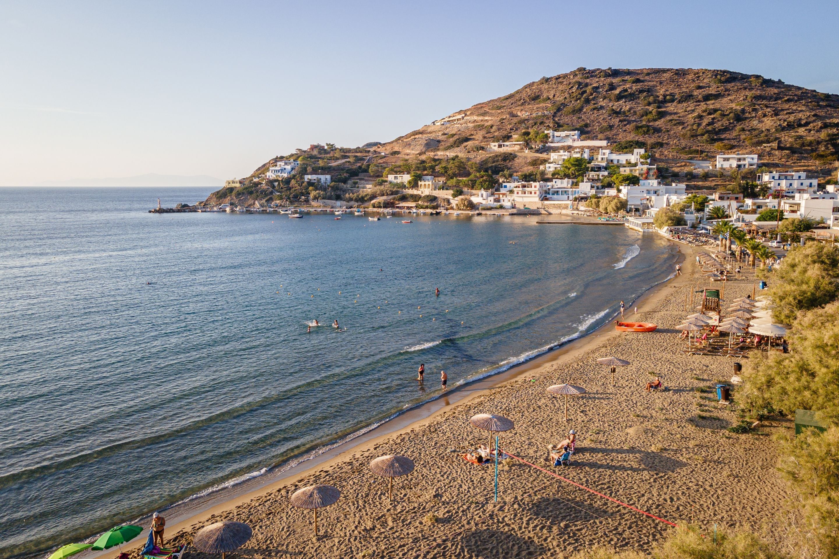 A beach with a clear view of the sea, a sandy shore, and buildings on a hillside.