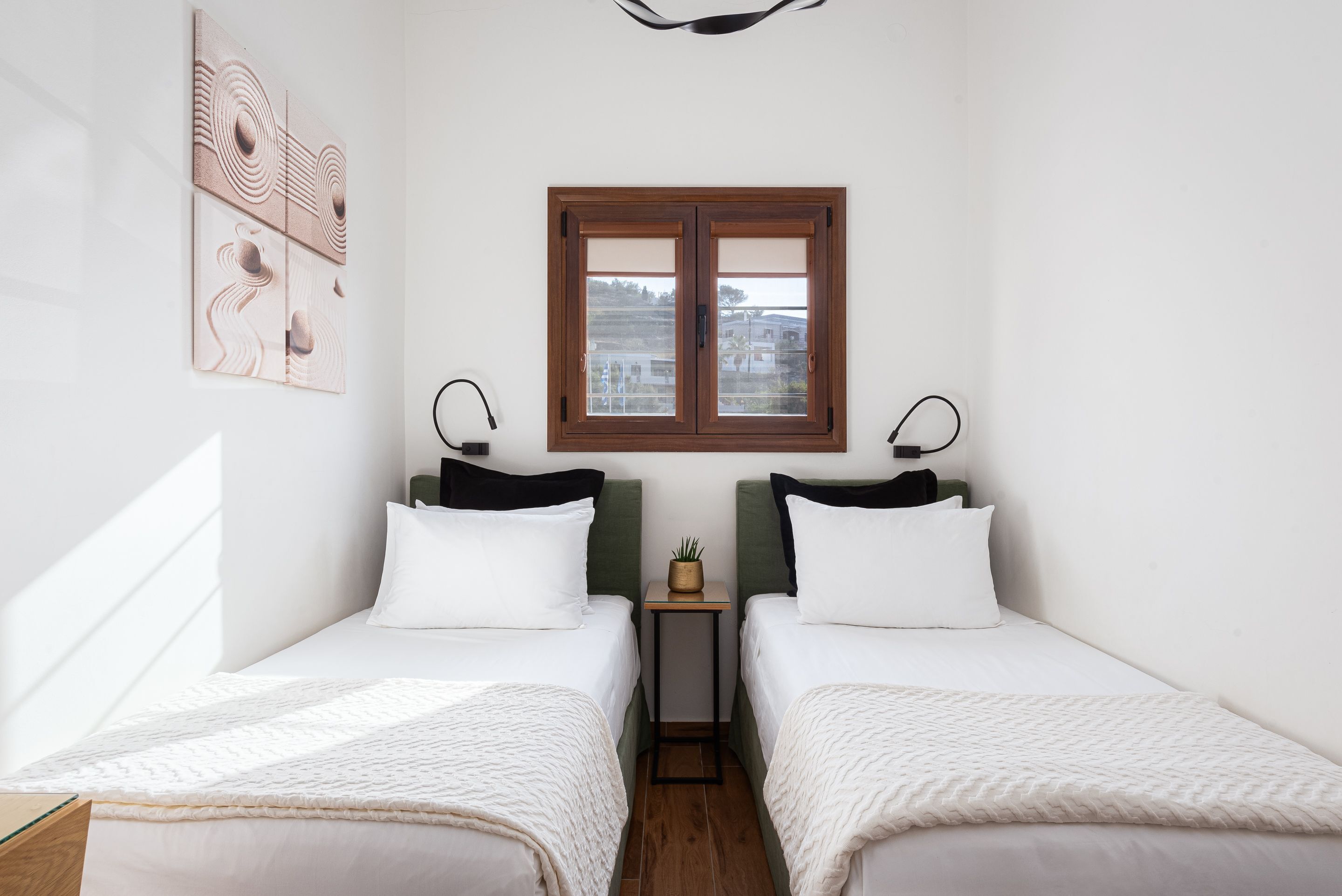 Quarto com duas camas, uma mesinha com uma planta e uma janela com vista.