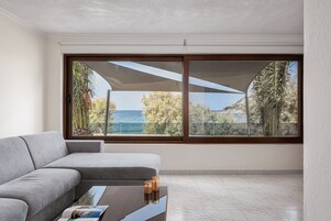 Un salón moderno con un sofá gris, una mesa de centro y vistas al mar a través de amplios ventanales.