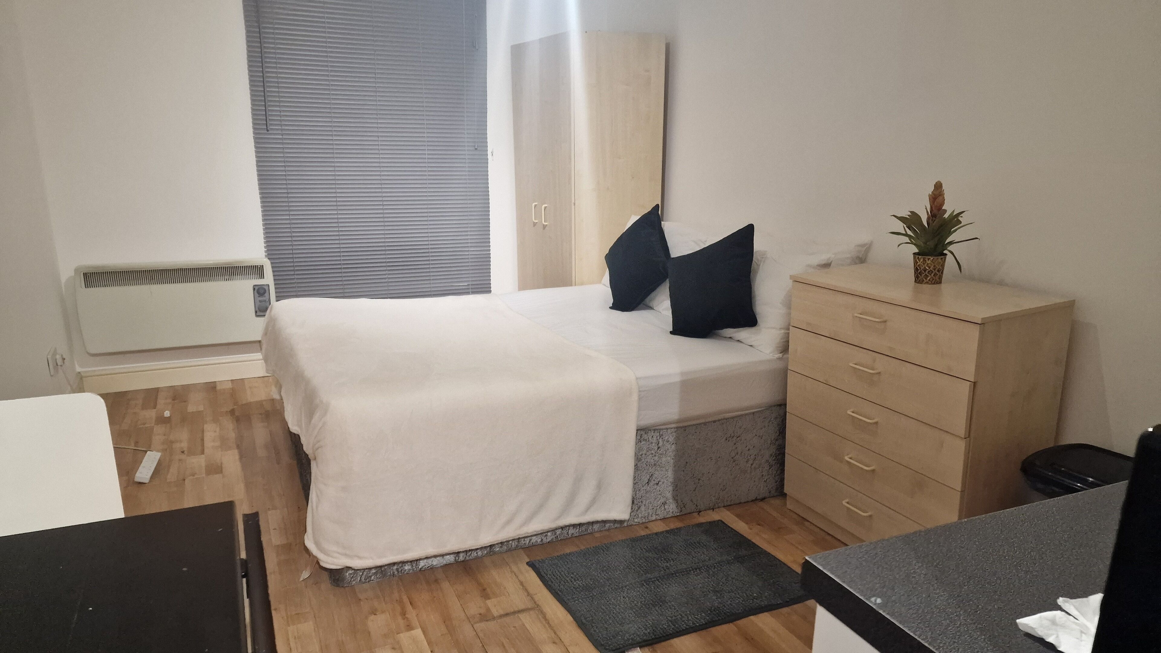A bedroom with a bed, a dresser, a radiator, and a window with blinds.