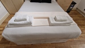 A neatly made bed with white linens and towels folded at the head. - Compact Living Cosy Studio Flat in London (London)