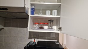 A kitchen with a microwave, a coffee maker, and a shelf with jars and a box. - Compact Living Cosy Studio Flat in London (London)