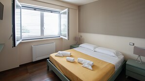 Een slaapkamer met een bed, nachtkastje, lamp, raam en radiator.