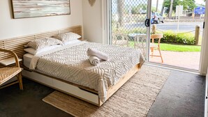 Ein Schlafzimmer mit Bett, Stuhl, einem Gemälde und Blick ins Freie.