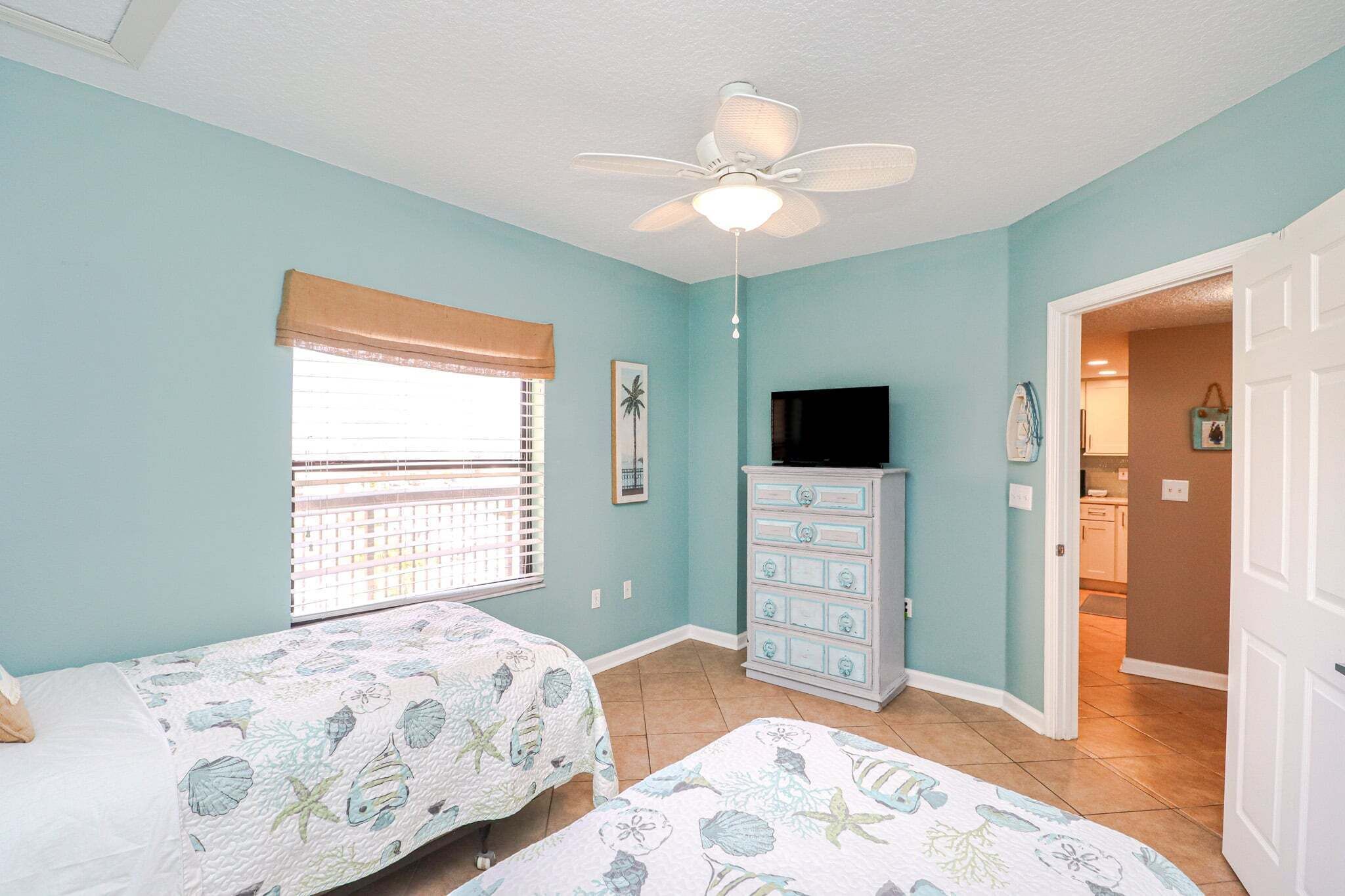 A bedroom with two beds, a ceiling fan, a dresser, and a television.