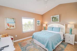 A bedroom with a bed, two bedside tables with lamps, a window with blinds, and artwork on the walls.