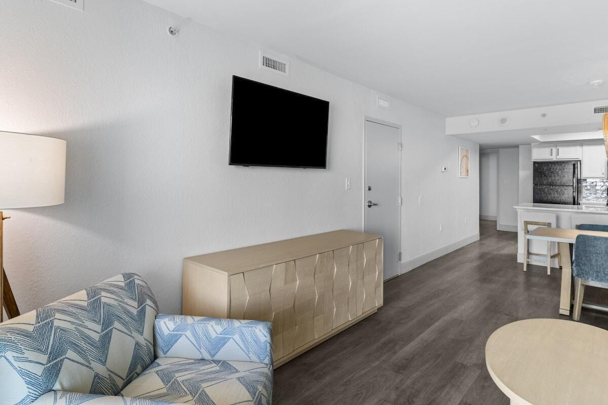 A modern living room with a sofa, a cabinet, a flat-screen TV, and a dining area with a table and chairs.