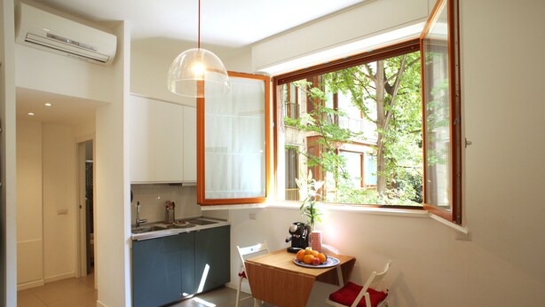 Una cucina compatta con zona pranzo, una finestra che si affaccia sul verde e una lampada a sospensione.