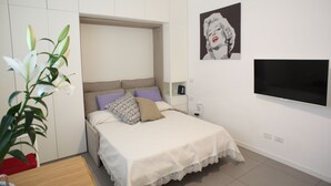 Una camera da letto con un letto, una TV, una pianta e un quadro appeso al muro.