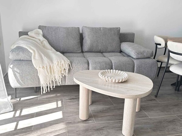 A modern living room with a grey sofa, a white throw blanket, and a round wooden coffee table.