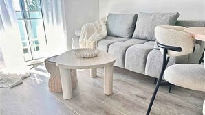 Ett modernt vardagsrum med en grå soffa, ett runt soffbord i trä och en fåtölj i rotting.