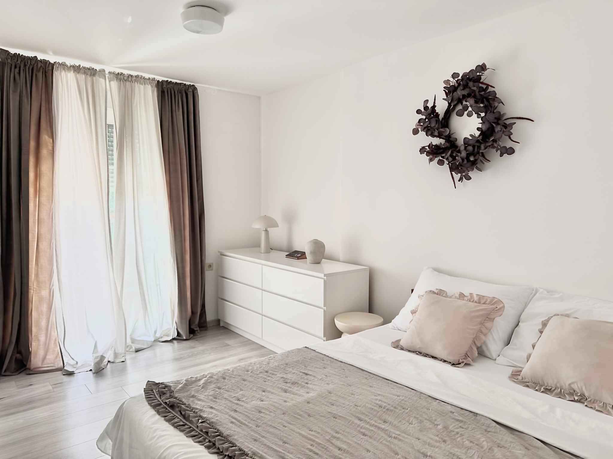 Un dormitorio con cama, mesita de noche, cómoda y un arreglo decorativo en la pared.