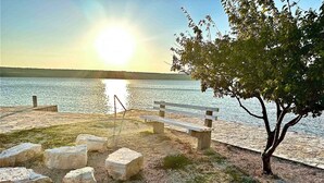 A lakeside park with a wooden bench and stone seating, a tree, and a clear view of the lake.