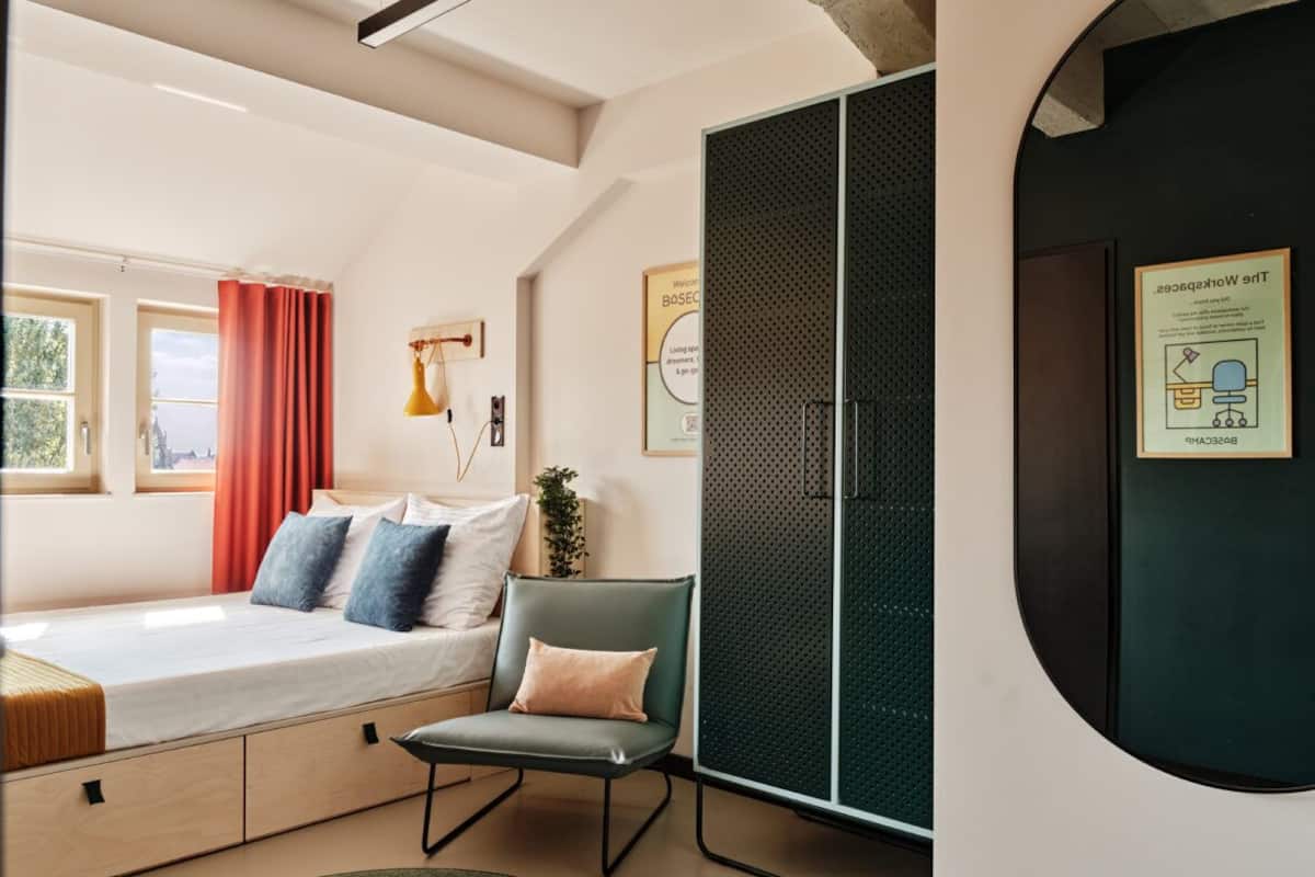 A modern bedroom with a bed, a chair, a wardrobe, and a circular window.