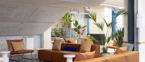 A modern lounge area with leather sofas, a patterned rug, and potted plants.