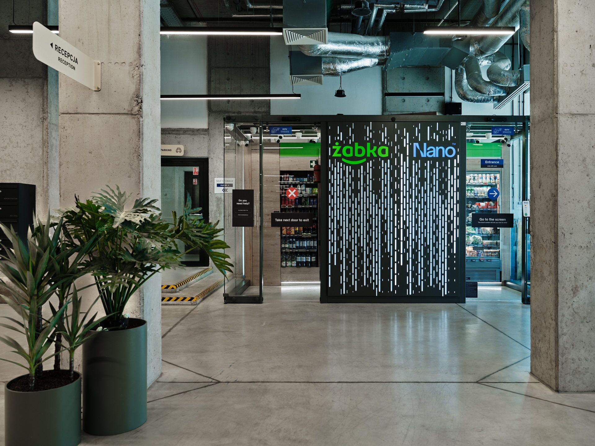 A reception area with a sign for 'RECEPTION' and a 'SELF STORAGE' sign. There are potted plants and a 'Nano' sign in the background.