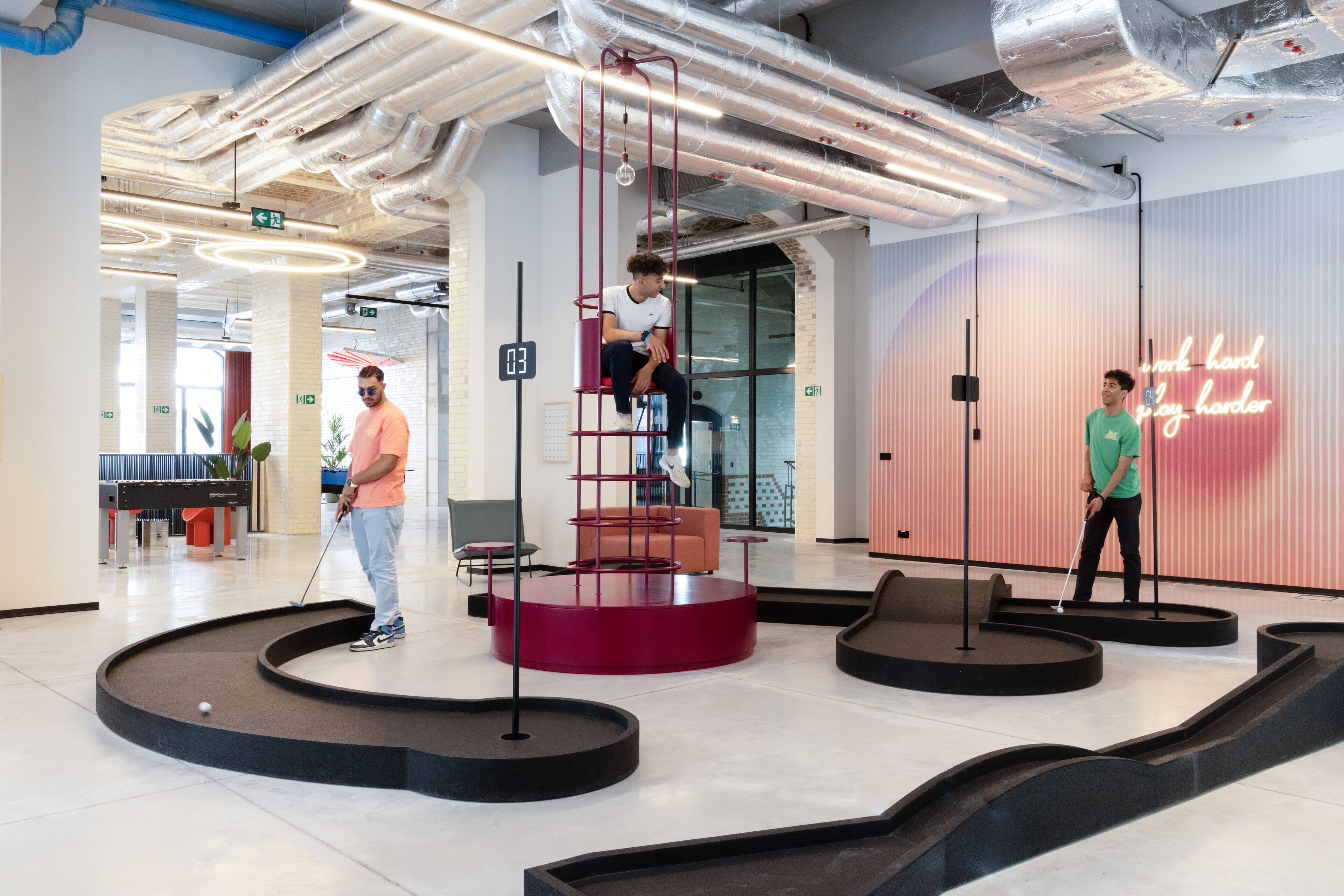 A modern indoor space with a pool table, a red circular platform, and a neon sign.