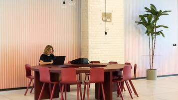 A conference room with a round table, red chairs, a laptop on the table, and a potted plant.