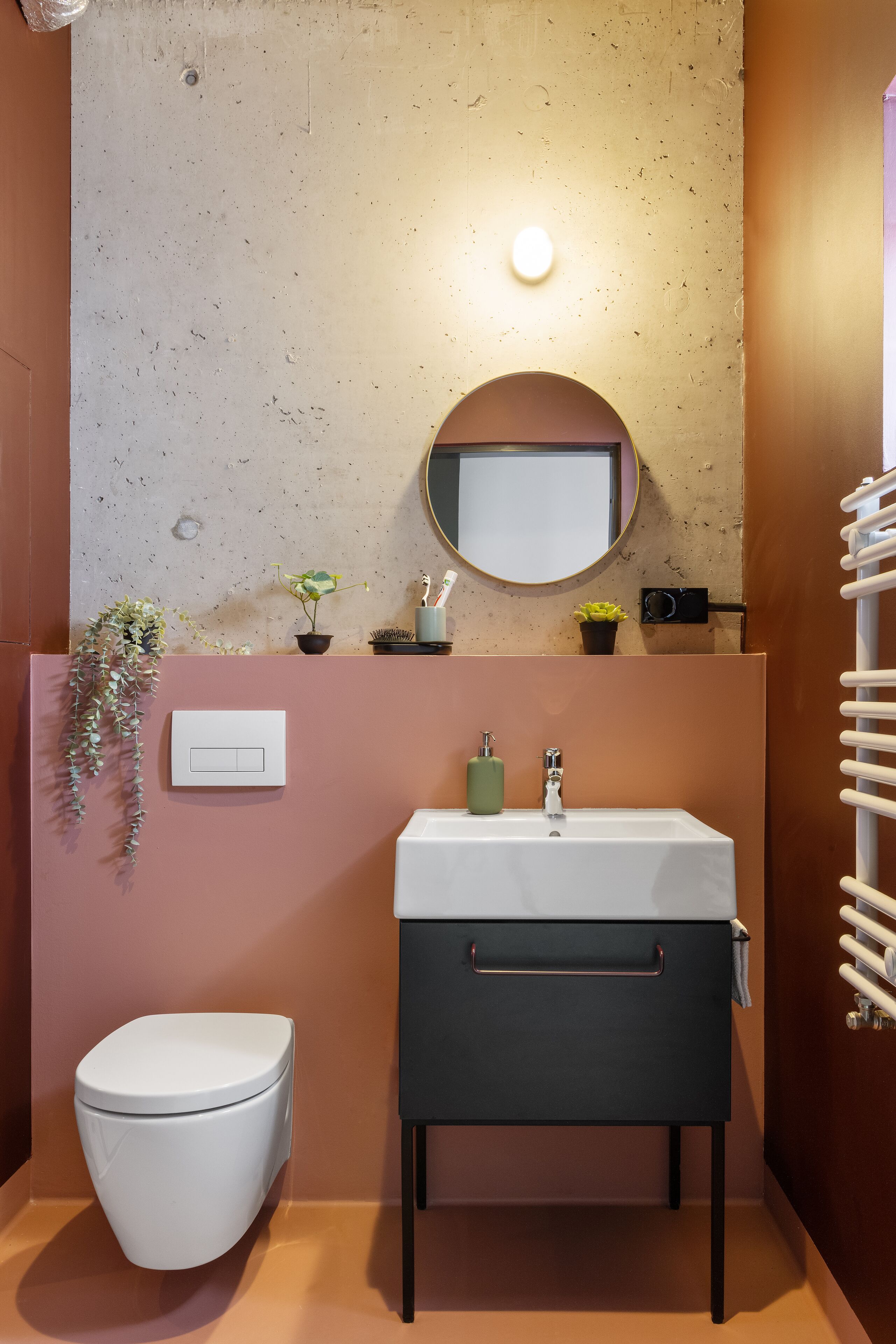 A bathroom with a white toilet, a dark vanity with a mirror, and a wall-mounted light fixture.