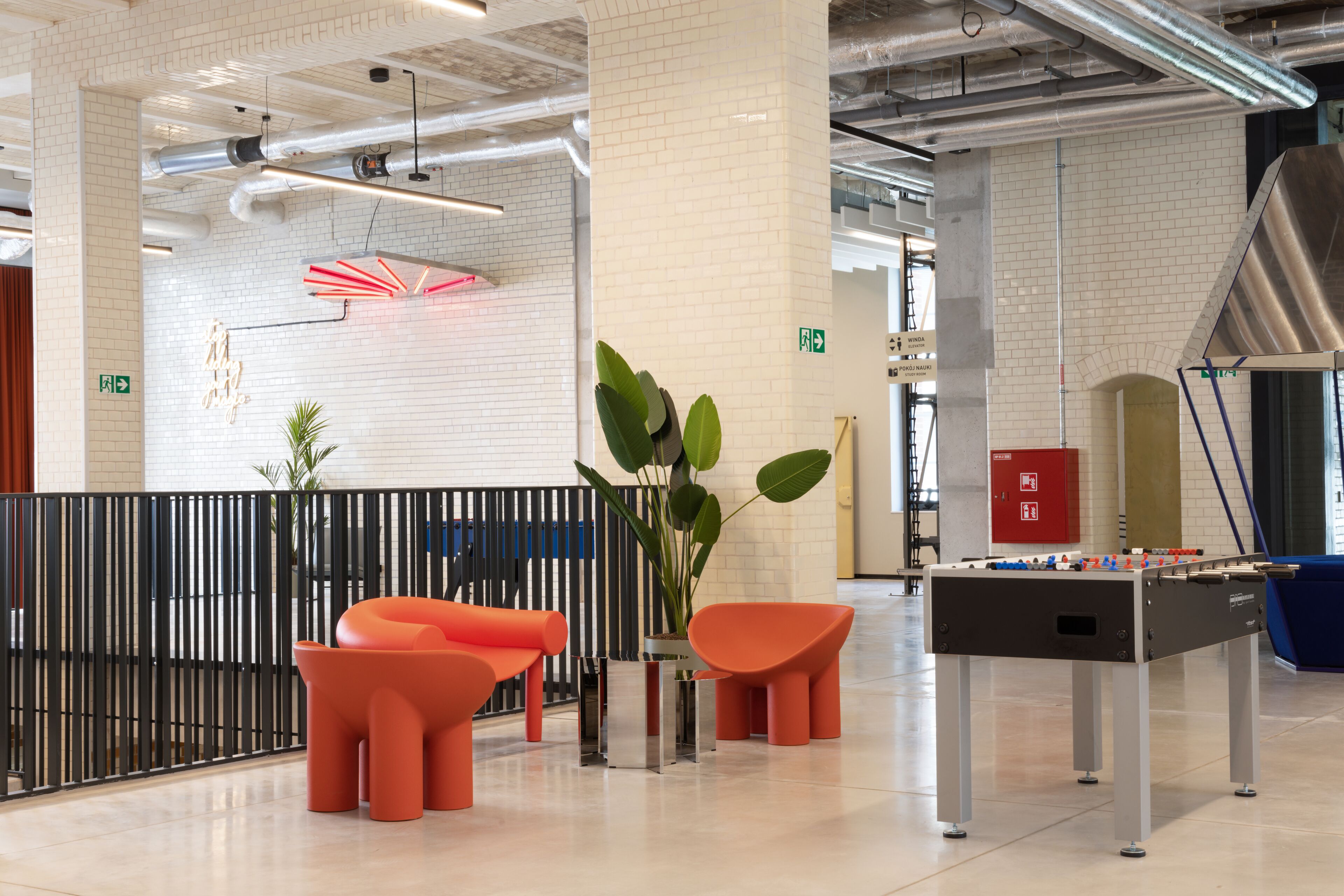 A modern lobby with a foosball table, orange seating, and a decorative wall with a geometric light fixture.