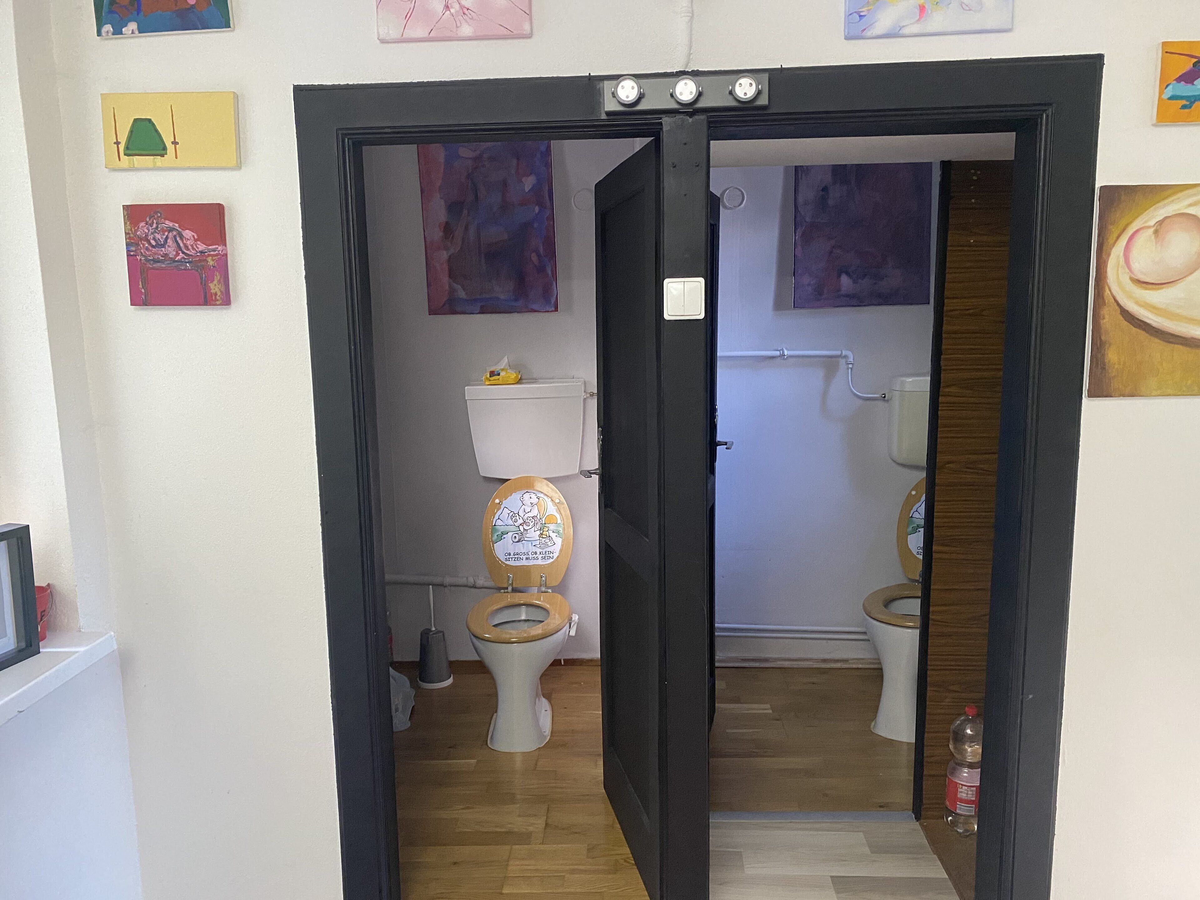 Ein Badezimmer mit zwei Toiletten, Holzboden und unterschiedlichen Wanddekorationen.