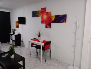 A modern room with a dining table, chairs, a TV, and abstract wall art. - Studio Apartment with Shared Pool, Wi-Fi and Air Conditioning (La Cala del Moral)