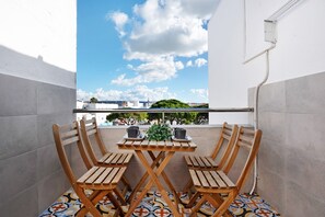 A balcony with a tiled floor, a wooden table with chairs, and a view of buildings and trees.