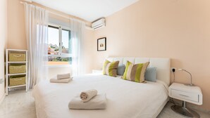 A bedroom with a large bed, bedside tables, a window with curtains, a wall-mounted air conditioner, and a small shelf with baskets. - Holiday Apartment "Penthouse 3-Bedroom Duplex" with Sea View, Shared Pool & Wi-Fi (Mijas)