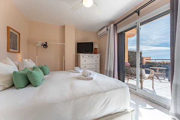 A bedroom with a bed, a television, a dresser, and a balcony with outdoor furniture.