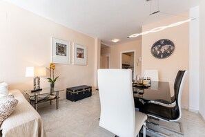 A modern hotel room with a bed, a glass table with a lamp, a chair, a world map clock, and framed pictures on the wall.