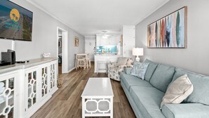 A modern living room with a TV, white cabinets, a light blue sofa, and a kitchen in the background. - Ocean Forest Villas Unit B305 - Ocean view (Myrtle Beach)