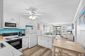 Une cuisine moderne avec des armoires blanches, un four à micro-ondes, une cuisinière et un ventilateur de plafond.