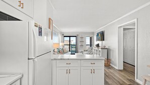 A modern kitchen with white cabinetry, a central island, and a view through the open door. - Ocean Forest Villas Unit B305 - Ocean view (Myrtle Beach)