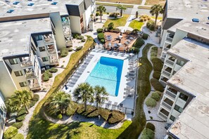 Vue aérienne d’un hôtel doté d’une piscine, de chaises longues et d’un jardin aménagé.