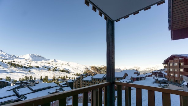 Un pueblo nevado en la montaña, con edificios y un balcón de madera, bajo un cielo despejado.