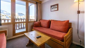 Una habitación con un sofá de madera, una mesita pequeña, una ventana con vistas a las montañas y una lámpara.